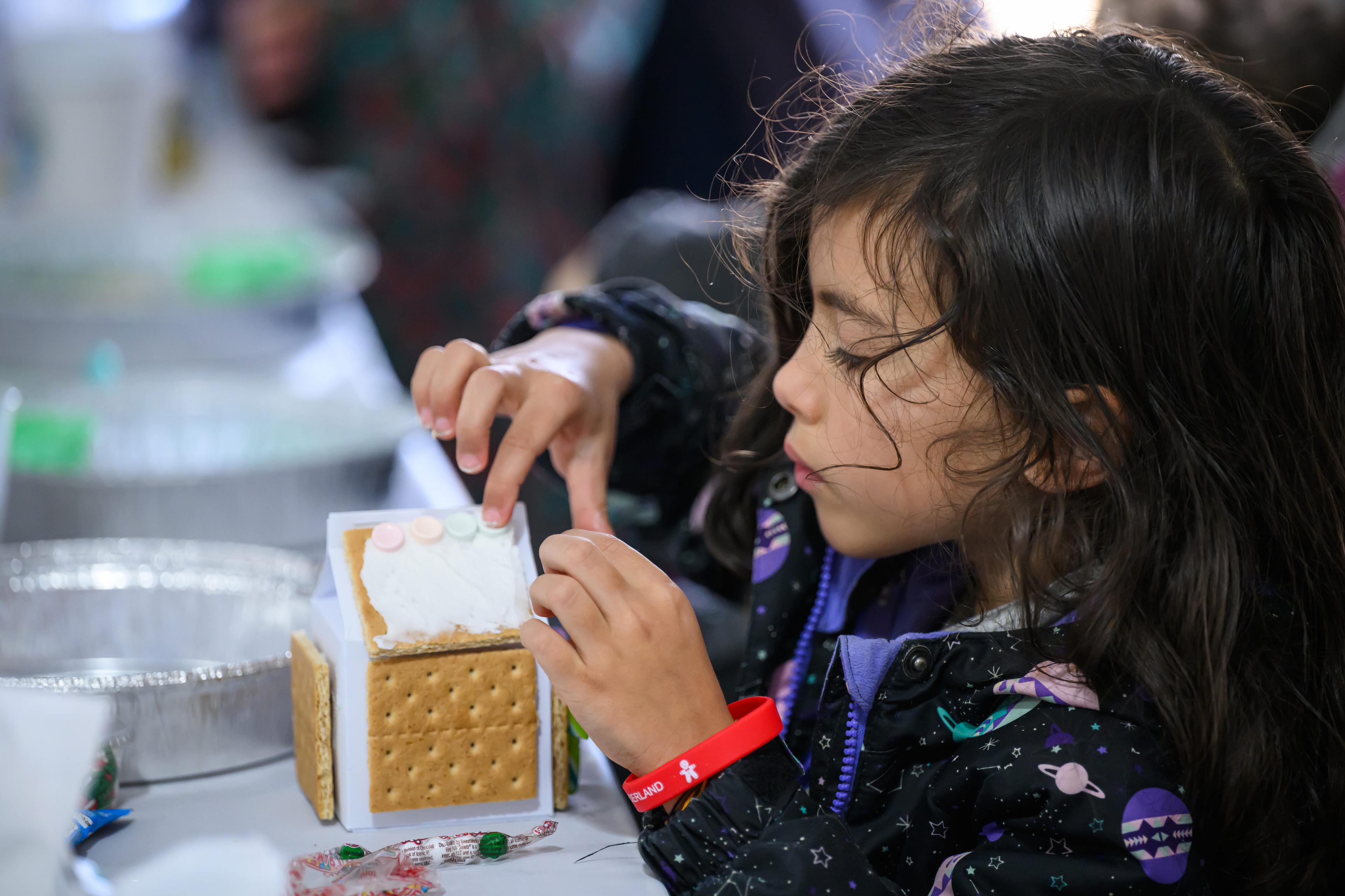 a small girl carefully crafting a gingerbread house